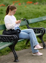 坐在公园椅子上看手机的少女图片